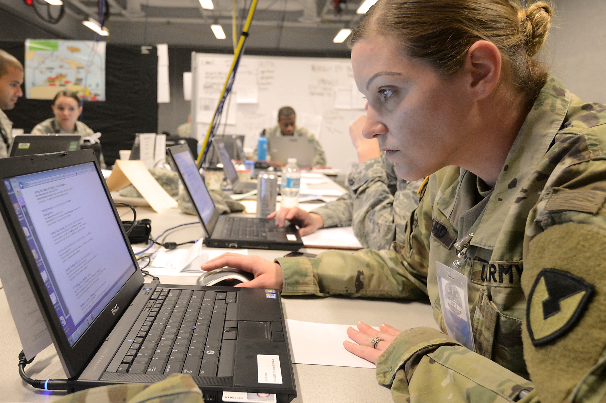 An Army contracting specialist reviews a laptop screen while colleagues work at adjacent computers